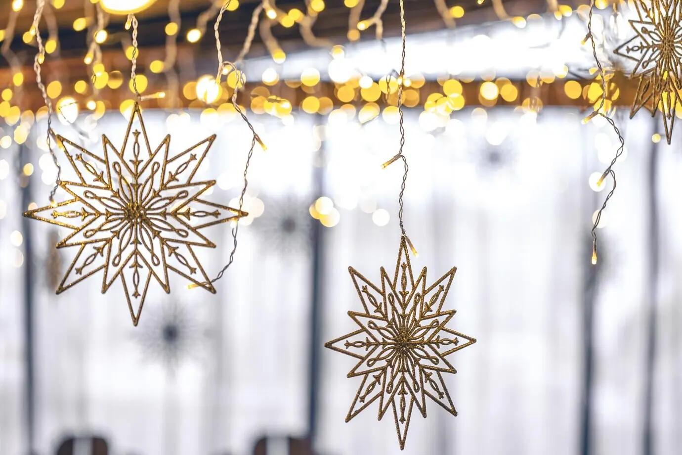 Dekorative Schneeflocken und Girlanden vor unscharfem Innenraumhintergrund